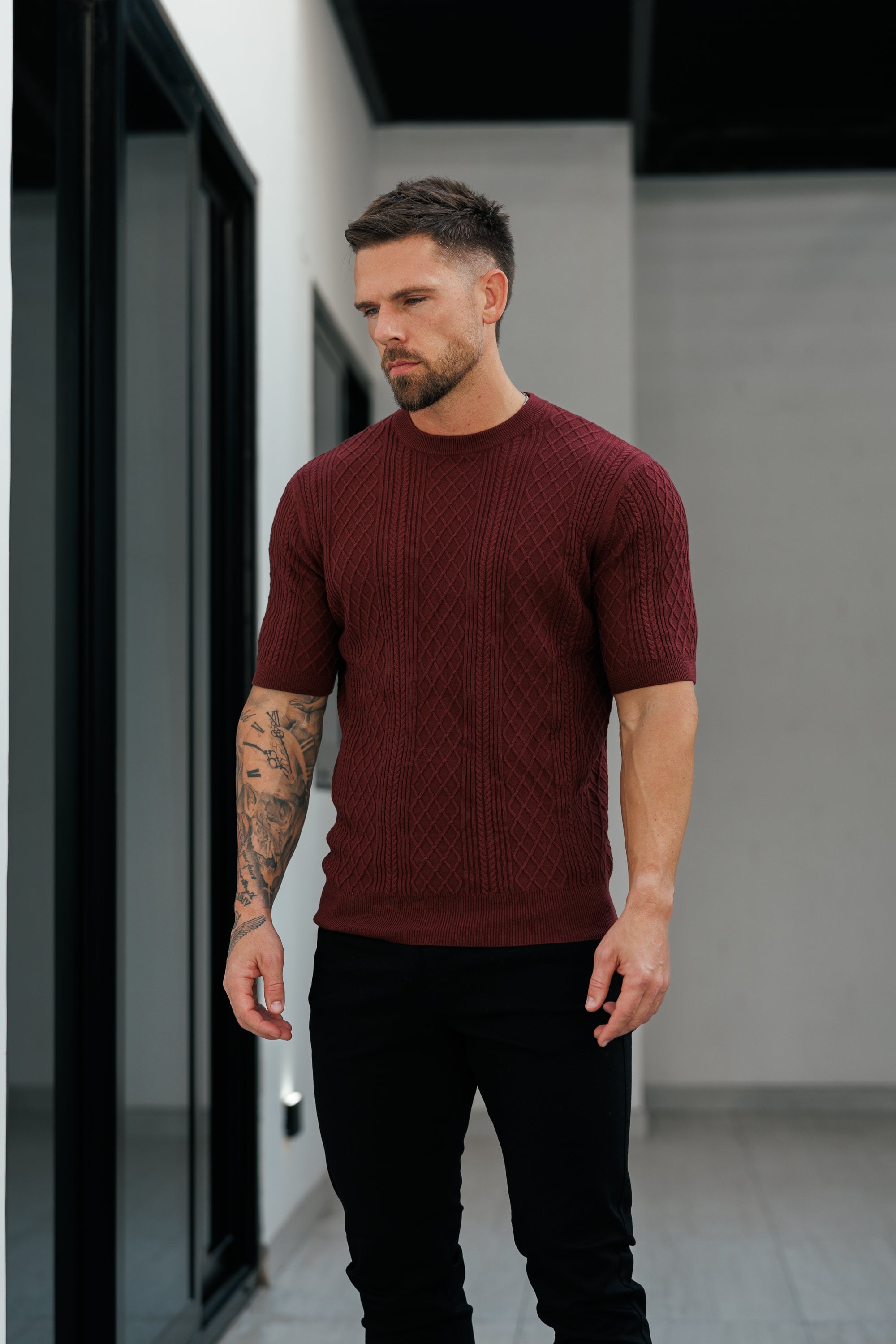 Man wearing a maroon sweater and black pants standing indoors.